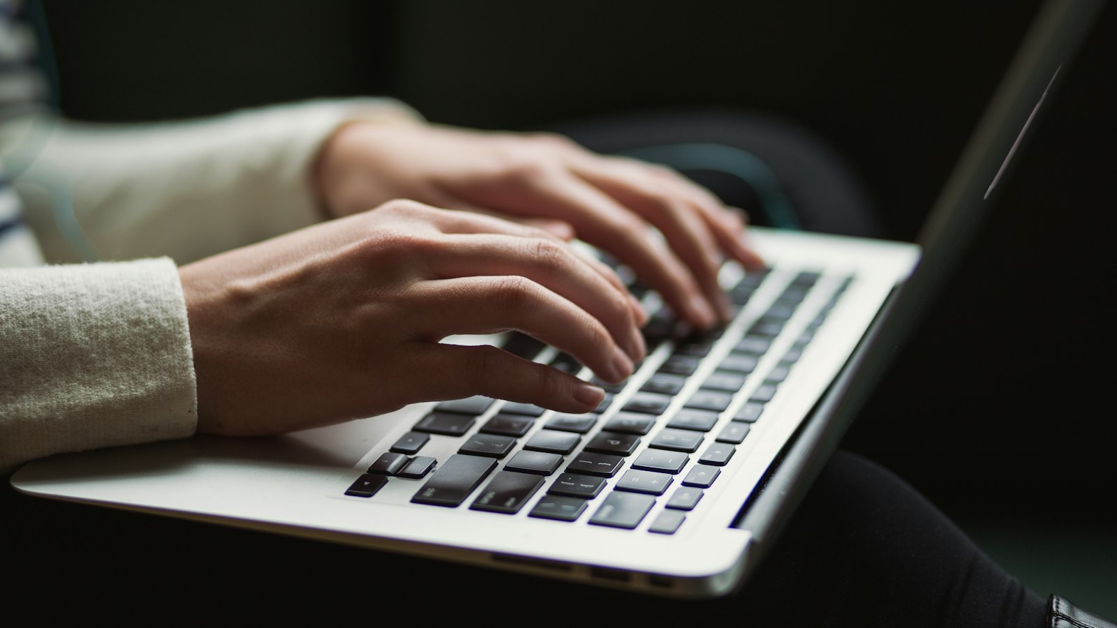 Orang mengetik di laptop di atas meja kayu yang gelap, dengan secangkir kopi di sampingnya